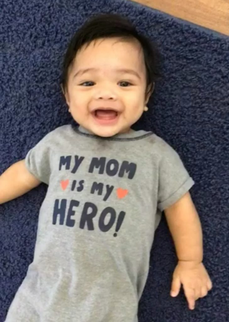 Baby Alexander smiling, wearing a onesie that reads, "My mom is my hero."