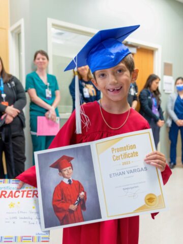 Ethan wearing a cap and gown and holding his kindergarten certificate at CHOC